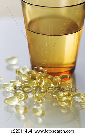 Evening primrose oil capsules in a pile next to a glass of water. View Large Photo Image Picture - Evening primrose oil capsules in a pile next to a glass of water.. Fotosearch