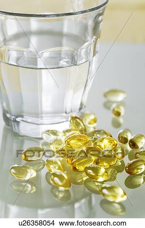Evening primrose oil capsules in a pile next to a glass of water. View Large Photo Image Picture - Evening primrose oil capsules in a pile next to a glass of water.. Fotosearch