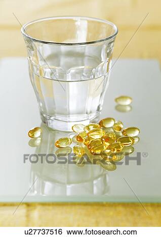 Stock Photograph - Evening primrose oil capsules in a pile next to a glass of water.. Fotosearch
