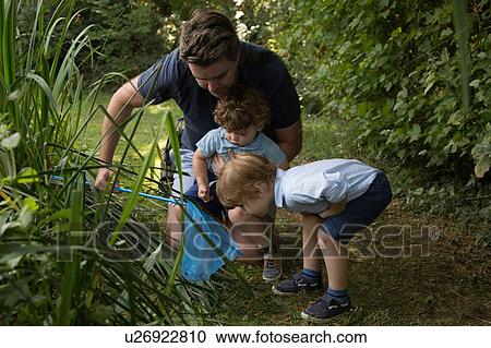 Stock Image - Father and children with fishing net in park. Fotosearch