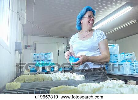 Stock Photo - Female cheesemaker looking back while 0eparing cheeses. Fotosearch