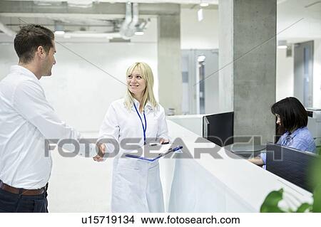 Female doctor shaking hands with male patient at hospital desk. View Large Photo Image Picture - Female doctor shaking hands with male patient at hospital desk.. Fotosearch