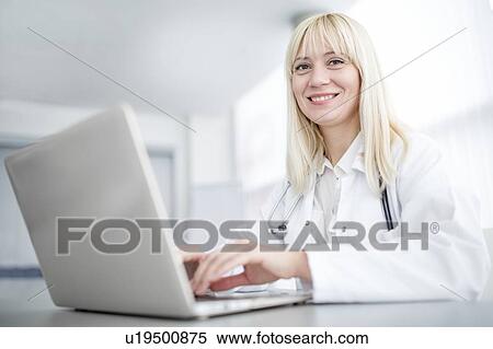 Stock Photography - Female doctor using laptop and smiling.. Fotosearch