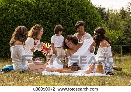 Stock Image - Female friends and family having picnic in garden. Fotosearch