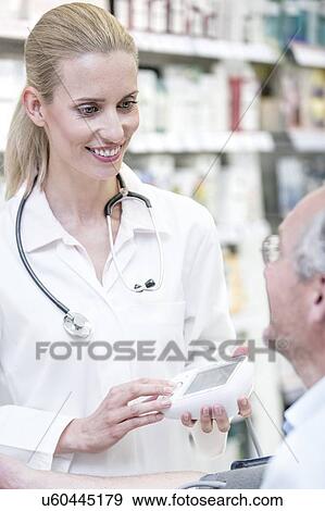 Stock Photo - Female pharmacist checking mature male patient's blood pressure in pharmacy.. Fotosearch