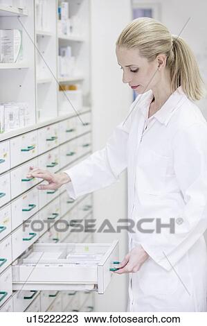 Stock Image - Female pharmacist looking for medicine in drawer cabinet in pharmacy.. Fotosearch