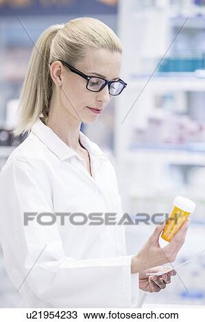 Stock Image - Female pharmacist reading label on pill bottle in pharmacy.. Fotosearch