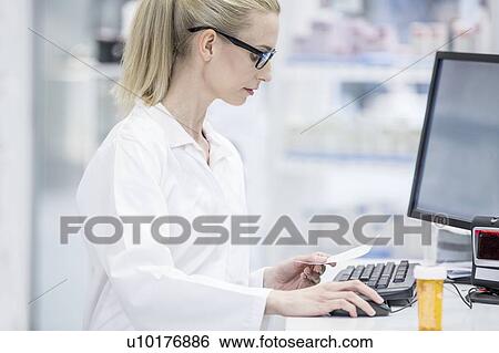 Stock Photograph - Female pharmacist working on computer in pharmacy.. Fotosearch