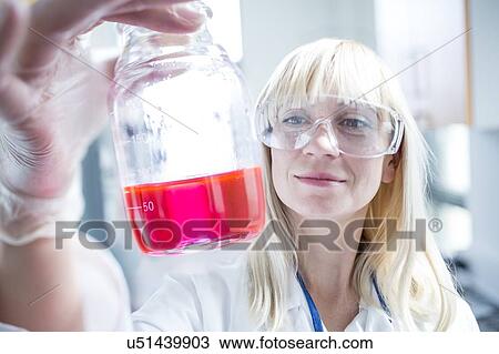 Stock Image - Female scientist wearing protective goggles and holding flask.. Fotosearch