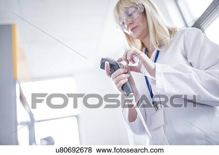 Stock Photo - Female scientist wearing protective goggles and using device.. Fotosearch