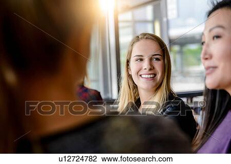 Stock Image - Female student friends chatting by university window. Fotosearch