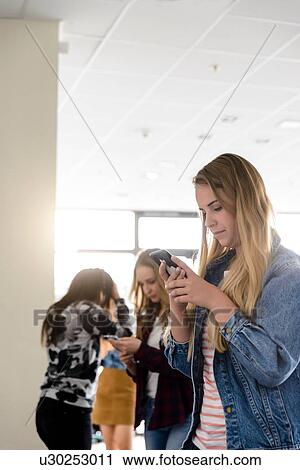 Female students looking at smartphones in university corridor View Large Photo Image Stock Image - Female students looking at smartphones in university corridor. Fotosearch