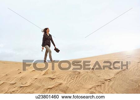 Stock Image - Female tourist walking barefoot on sand dune, Las Palmas, Gran Canaria, Canary Islands, Spain. Fotosearch