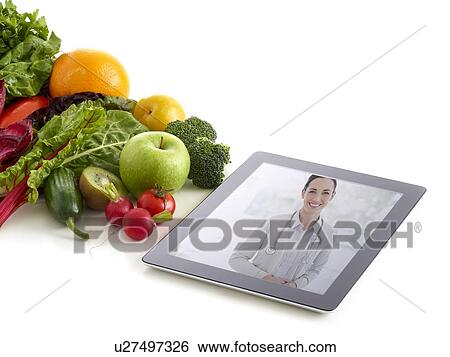 Stock Photograph - Fresh fruit and vegetables with doctor's image on digital tablet, studio shot.. Fotosearch