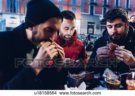 Friends enjoying burger at outdoor cafe, Milan, Italy View Large Photo Image Picture - Friends enjoying burger at outdoor cafe, Milan, Italy. Fotosearch