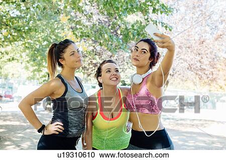 Stock Image - Friends exercising and taking selfie in park. Fotosearch