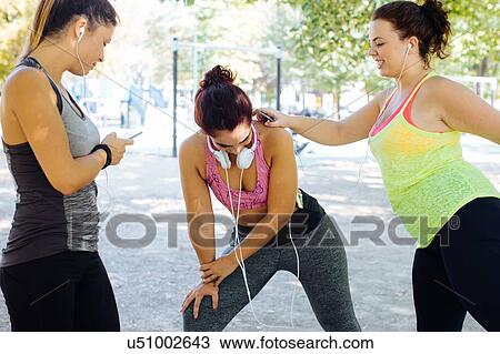 Stock Image - Friends exercising and using cellphone in park. Fotosearch