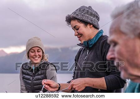 Stock Image - Friends having dinner by lakeside, Johnstone Strait, Telegraph Cove, Canada. Fotosearch