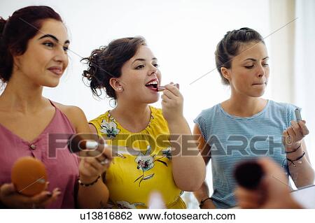 Stock Image - Friends putting on makeup at mirror. Fotosearch