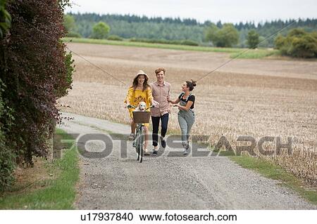 Stock Image - Friends running along by pushbike in countryside. Fotosearch