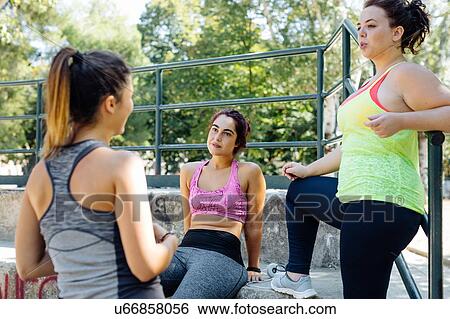 Stock Photograph - Friends taking break from exercise in park. Fotosearch