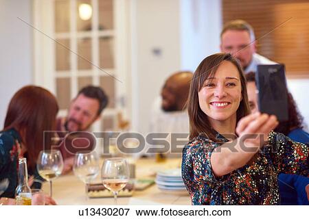 Stock Photo - Friends taking selfie at dinner party. Fotosearch