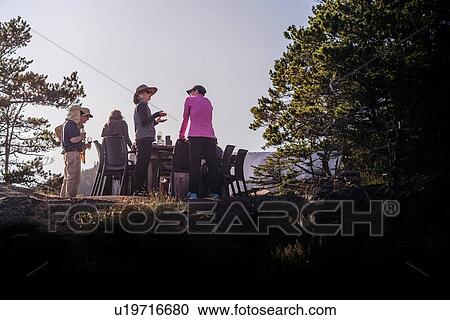 Stock Image - Friends talking at dinner on cliff top, Johnstone Strait, Telegraph Cove, Canada. Fotosearch
