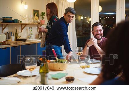 Stock Image - Friends talking, man setting table at dinner party. Fotosearch