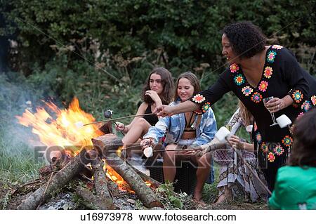 Stock Photo - Friends toasting marshmallows at bonfire party in park. Fotosearch