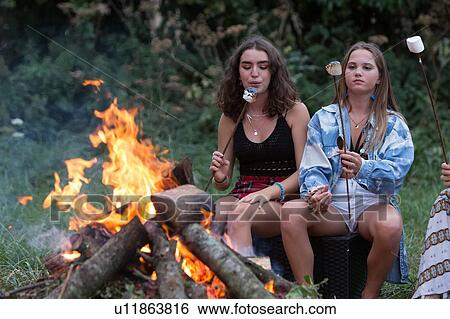 Stock Photograph - Friends toasting marshmallows at bonfire party in park. Fotosearch