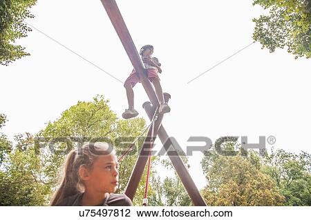 Stock Image - Girl below boy on playground equipment. Fotosearch
