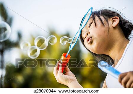 Girl blowing bubbles with bubble wand in park. View Large Photo Image Picture - Girl blowing bubbles with bubble wand in park.. Fotosearch