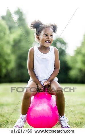 Stock Photograph - Girl bouncing on inflatable hopper in park, laughing.. Fotosearch