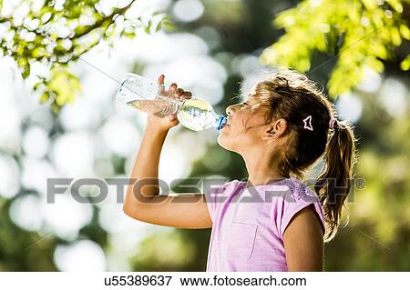 Stock Photo - Girl drinking water from plastic bottle in park.. Fotosearch