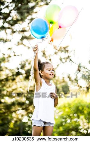 Stock Photography - Girl holding bunch of balloons in park.. Fotosearch