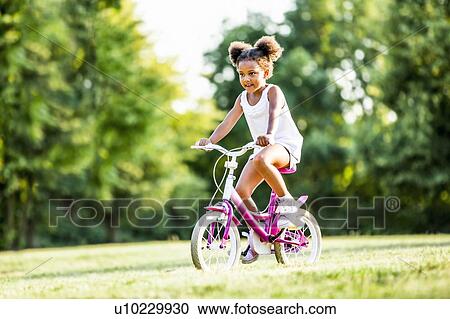 Stock Image - Girl in bunches riding bicycle in park.. Fotosearch