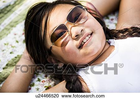Stock Image - Girl lying on blanket in park, smiling, portrait.. Fotosearch