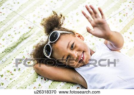 Stock Image - Girl lying on blanket in park, smiling, portrait.. Fotosearch