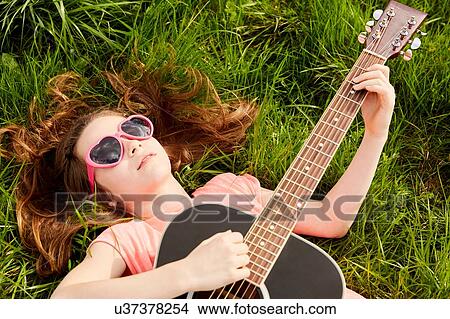 Picture - Girl playing guitar on grass. Fotosearch