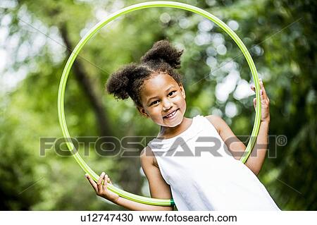 Stock Image - Girl playing with hula hoop in park, smiling, portrait.. Fotosearch