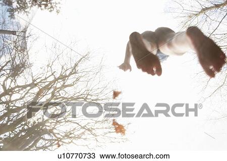 Stock Image - Girl standing barefoot on trampoline, low angle view. Fotosearch