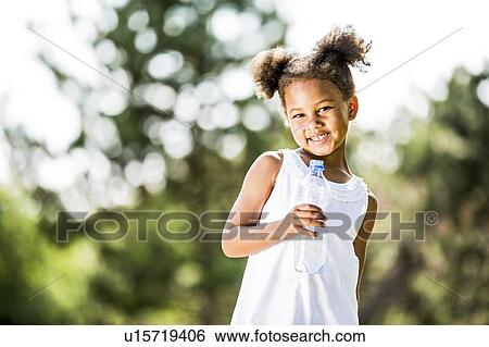 Stock Photograph - Girl standing with water bottle in park, smiling, portrait.. Fotosearch