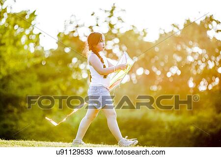 Stock Image - Girl walking with kite in park.. Fotosearch