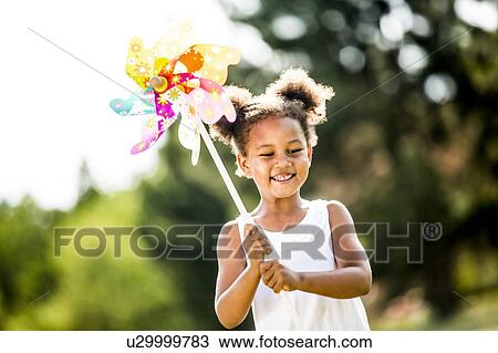Stock Image - Girl with bunches holding windmill, smiling.. Fotosearch