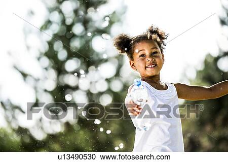 Girl with bunches splashing water from plastic bottle, smiling. View Large Photo Image Stock Image - Girl with bunches splashing water from plastic bottle, smiling.. Fotosearch