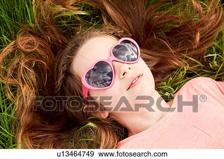 Girl with heart shaped sunglasses lying on grass View Large Photo Image Stock Photo - Girl with heart shaped sunglasses lying on grass. Fotosearch