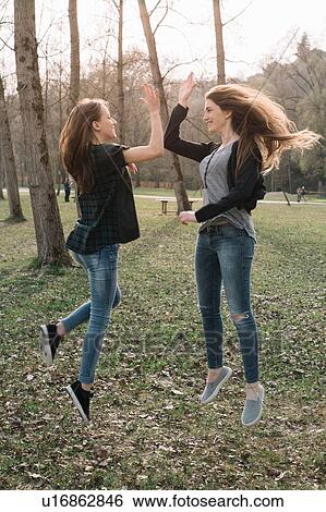 Stock Photograph - Girlfriends jumping and doing high five in park. Fotosearch