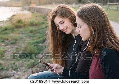 Picture - Girlfriends listening to music in park. Fotosearch