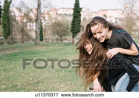 Stock Photo - Girlfriends playing piggyback ride in park. Fotosearch