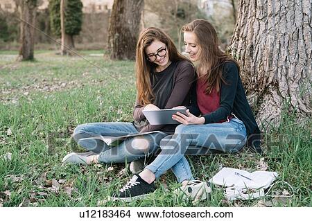 Picture - Girlfriends reading book in park. Fotosearch